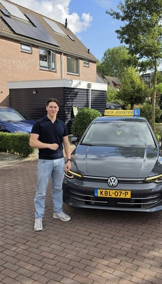 Guus steekt zijn duim op naast de lesauto na zijn examen