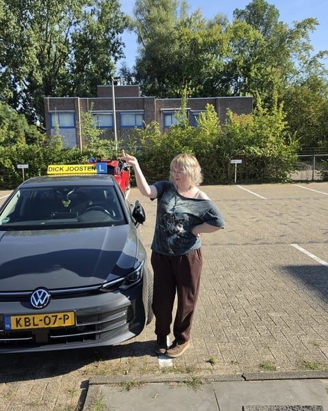 Iza naast de grijze VW Golf-lesauto na haar examen