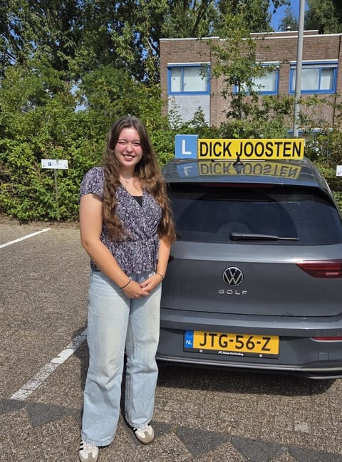 Jillana naast de grijze VW Golf-lesauto na haar examen