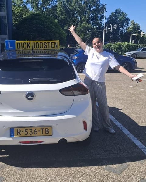 Yuna juicht naast de witte Opel Corsa-lesauto na haar examen