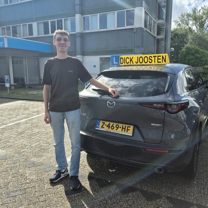 Sam naast de grijze Mazda-lesauto na zijn examen