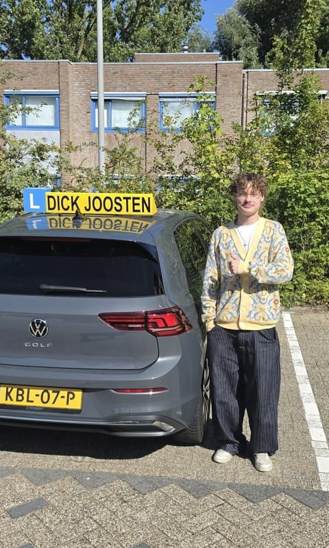 Luke steekt zijn duim op naast een van onze lesauto's, na zijn examen